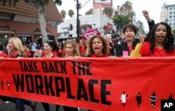 FILE - Participants, holding a sign protesting sexual harassment and assaults in the workplace, walk at the #MeToo March in the Hollywood section of Los Angeles, California, Nov. 12, 2017.