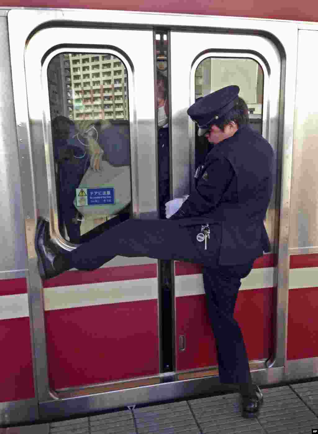 일본 도쿄 가와사키 전철역에서 만원 열차에 타려는 승객의 옷이 문에 끼자, 역무원이 문을 잡고 버티고 있다.