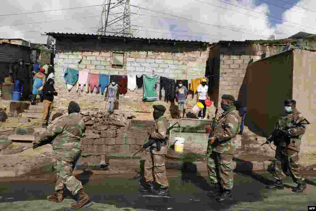 People stand near their home and watch as members of the South African Defence Force patrol their area in Alexandra township, Johannesburg. Stores and warehouses in South Africa were hit by looters on July 13. 