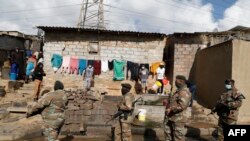 Watu wasimama karibu na nyumba zao wakiwatizama wanajeshi wa Afrika Kusini wakishika doria katika eneo lao katika kitongoji cha Alexandria, Johannesburg, Julai 15, 2021. Picha ya AFP 