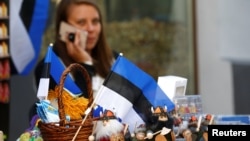 FILE - An Estonian national flag is seen as a street vendor speaks on her phone in Tallinn, Estonia, May 31, 2018.