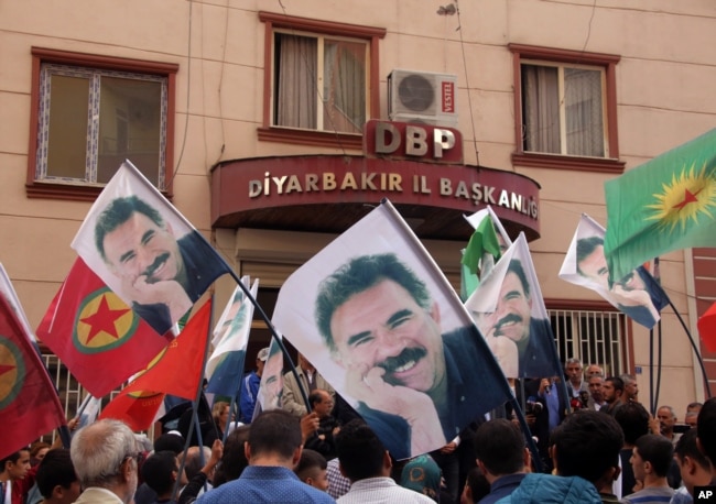 FILE - People hold posters of jailed PKK leader Abdullah Ocalan and PKK flags as they gather outside the headquarters of pro-Kurdish Democratic Regions Party, DBP, on the17th anniversary of Ocalan's expulsion from Syria, in Diyarbakir, Turkey, Oct. 9, 2015.