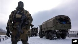 A pro-Russian rebel guards road near Donetsk airport with Ukrainian military vehicles at rear, Eastern Ukraine, Jan. 6, 2015.