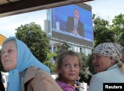 FILE - People wait for a boat next to an electronic screen showing live nationwide broadcasted call-in attended by Russian President Vladimir Putin, at Artillery Bay in the Black Sea port of Sevastopol, Crimea, June 15, 2017.