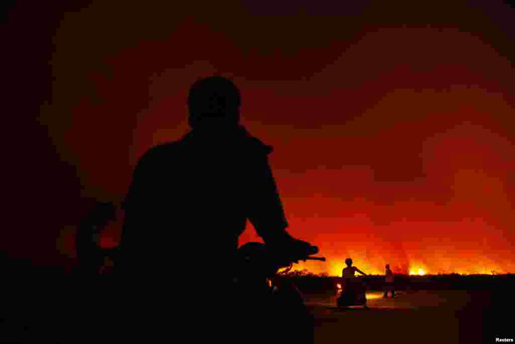 Villagers sit on their motorcycles as they get ready to leave their homes as a fire burns a palm oil plantation in Bangko Pusako district, Indonesia, June 22, 2013.