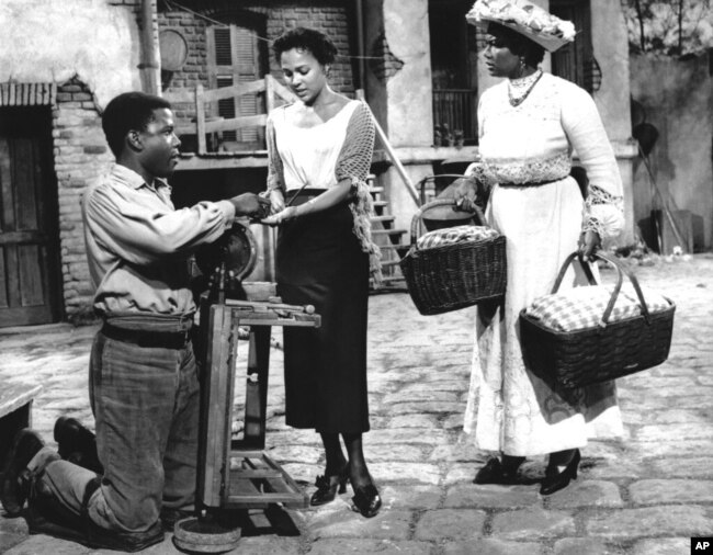 ARCHIVO - Arrodillado sobre sus piernas lisiadas, Porgy, interpretado por Sidney Poitier, insta a Bess (Dorothy Dandridge, en el centro) a unirse a Maria (Pearl Bailey) en el picnic, en esta escena de la versión cinematográfica de "Porgy and Bess", nov. 17 de febrero de 1958.