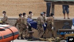 Des soldats italiens portent des sacs mortuaires d'une personne morte par naufrage à l'île de Lampedusa, en Italie, le dimanche 6 octobre 2013.