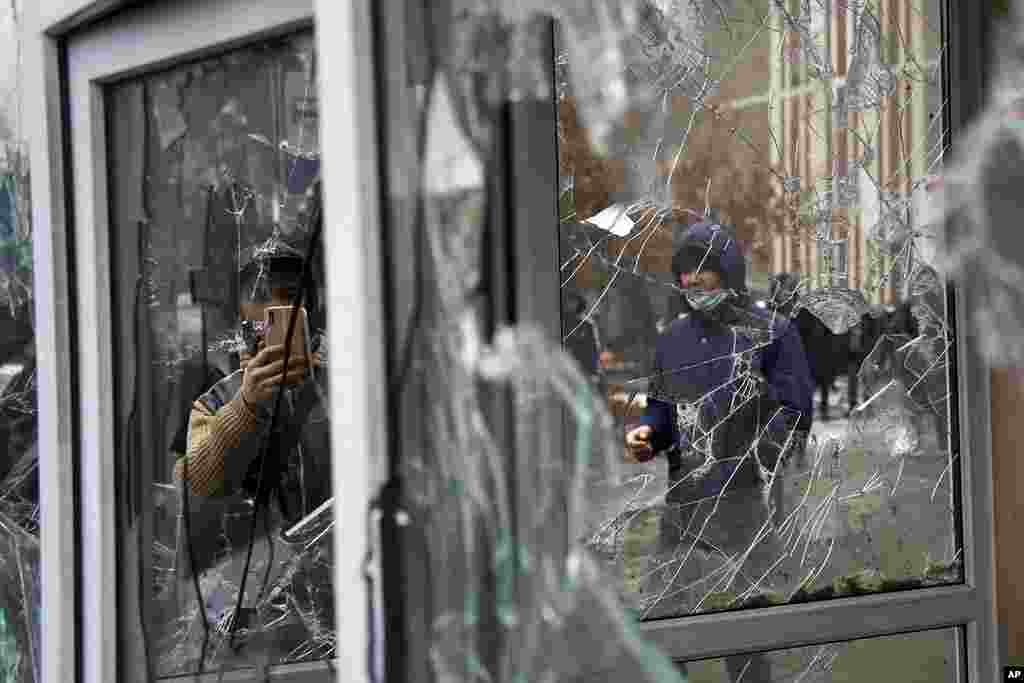 A man takes a photo of windows of a police kiosk damaged by demonstrators during a protest in Almaty, Kazakhstan.