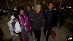 2013年11月6日，盲人法律维权人士陈光诚的母亲王金香（中）在另一个儿子陈光福（右）和他们的朋友周莉（左）的搀扶下抵达北京首都机场。王金香与陈光福乘飞机前往纽约和陈光诚团聚。 