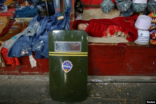 A child sleeps as a riot shield leans on a stall at the bazaar in Hotan, Xinjiang Uighur Autonomous Region, China, March 21, 2017.