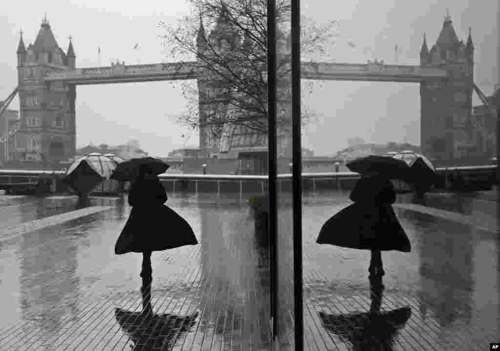 A woman is reflected in a window as she braves wind and rain while walking towards Tower Bridge in London during England&#39;s third national lockdown to curb the spread of coronavirus.