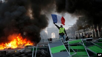 Một người biểu tình đứng trên hàng rào chướng ngại vật trên Đại lộ Champs-Élysées trong một cuộc biểu tình chống giá nhiên liệu gia tăng, ngày 24 tháng 11, ở Paris.