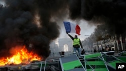 FILE - A demonstrator waves the French flag onto a burning barricade on the Champs-Elysees avenue during a demonstration against the rising of the fuel taxes, Nov. 24, 2018 in Paris.