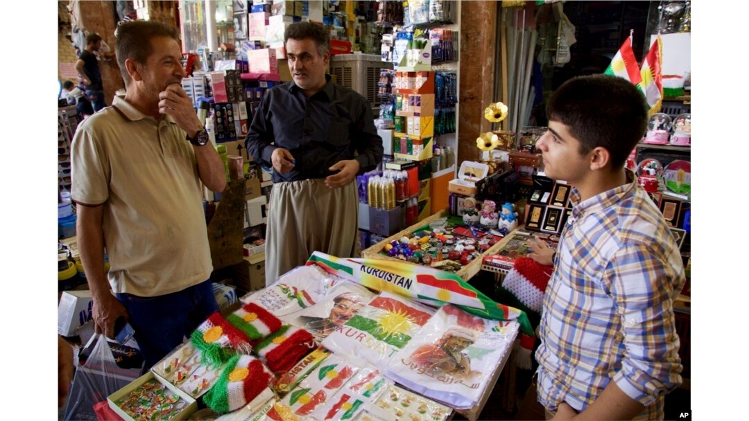 FILE - A salesman, talking to a customer, sells patriotic and pro-independence paraphanelia at a bazaar in Irbil, Iraq, Aug. 24, 2017.