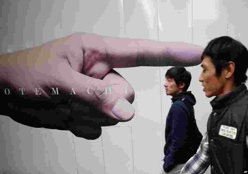 Men pass an advertisement posted on the fence of a construction site in Tokyo&#39;s Otemachi business district, Japan.