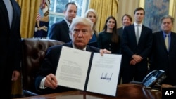 President Donald Trump shows his signature on an executive order on the Keystone XL pipeline, Jan. 24, 2017, in the Oval Office of the White House.