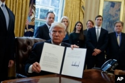 FILE - President Donald Trump shows his signature on an executive order on the Keystone XL pipeline, Jan. 24, 2017, in the Oval Office of the White House.