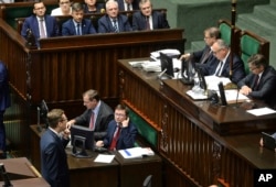 Polish Prime Minister Mateusz Morawiecki, upper left, looks on as a lawmaker for Poland's extreme right, Robert Winnicki, lower left, blocks the parliament's podium in a failed attempt to obstruct a vote on canceling penal provisions in Poland's Holocaust speech law, at the parliament in Warsaw, June 27, 2018.