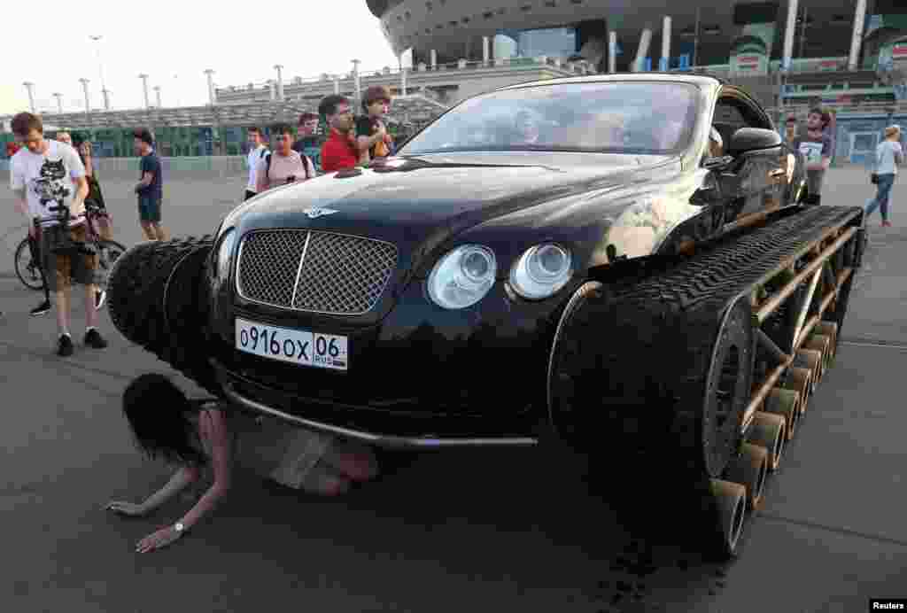 A woman poses for a picture with a caterpillar-tracked Bentley Continental GT, which was modified by Russian car engineering enthusiasts, during a demonstration in St. Petersburg, Russia.