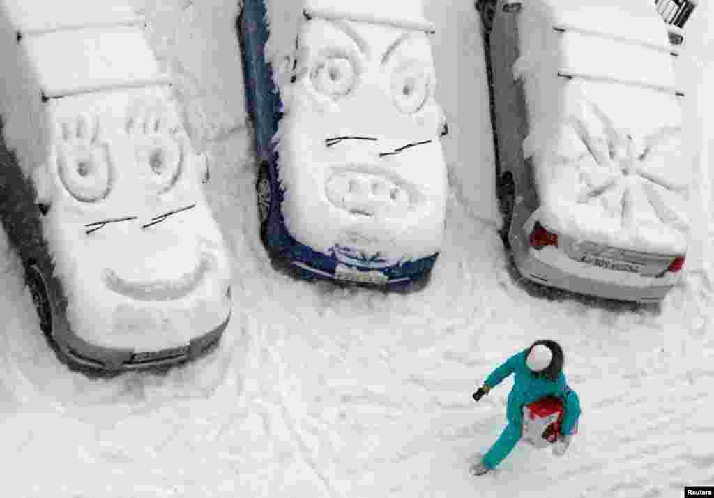 A woman walks past cars with faces which are scrawled on windows covered with snow during snowfall in Krasnoyarsk, Russia.