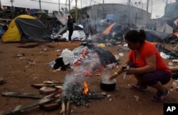 A woman makes instant coffee over a campfire a day beside belongings soaked in rains which continued overnight, inside the Benito Juarez sports complex in Tijuana, Mexico, Nov. 30, 2018.