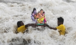 Orang-orang membawa patung dewa Hindu Ganesha, dewa kemakmuran dan melarungnya di lepas pantai laut Arab, selama festival Ganesh Chaturthi di Mumbai, India, 11 September 2021. (REUTERS/Francis Mascarenhas)