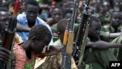 Fusil en main, des jeunes gens sont assis lors d’une cérémonie de désarmement, de démobilisation et de réinsertion d'enfants soldats à Pibor, État de Jonglei, au Soudan du Sud, sous la supervision de l'UNICEF et ses partenaires, le 10 février 2015.