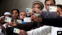Afghan men display their identification cards as the wait to cast their votes outside a polling station in Kabul, Afghanistan, Saturday, June 14, 2014.