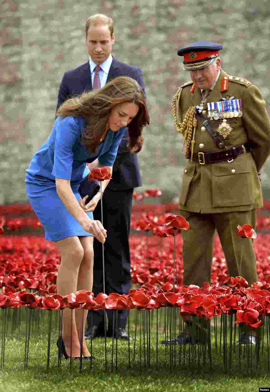 Britain&#39;s Catherine, Duchess of Cambridge, plants a ceramic poppy watched Prince William and Richard Dannatt (R) at the Tower of London&#39;s &#39;&quot;Blood Swept Lands and Seas of Red&quot; poppy installation to commemorate the 100th anniversary of World War I.