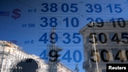 FILE - A woman is reflected in a window with a board displaying currency exchange rates in St. Petersburg, Russia.