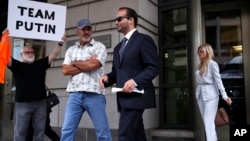 Former Donald Trump presidential campaign adviser George Papadopoulos, center, whose actions triggered the Russia investigation and who pleaded guilty to one count of making false statements to the FBI, leaves federal court with wife Simona Mangiante, right, after he was sentenced to 14 days behind bars, Sept. 7, 2018, in Washington. A protester is seen far left.