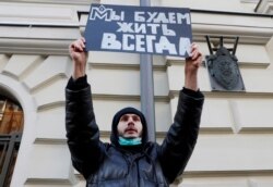 A supporter of the human rights group International Memorial holds a placard reading 'We will live forever' outside a court building during a hearing of the Russian Supreme Court to consider the closure of International Memorial in Moscow, Dec. 28, 2021.