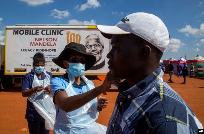 Un trabajador de la salud controla la temperatura de un hombre en cuarentena en una cancha de fútbol para detectar el COVID-19 en Lenasia South, sur de Johannesburg, Sudáfrica, el 21 de abril de 2020,