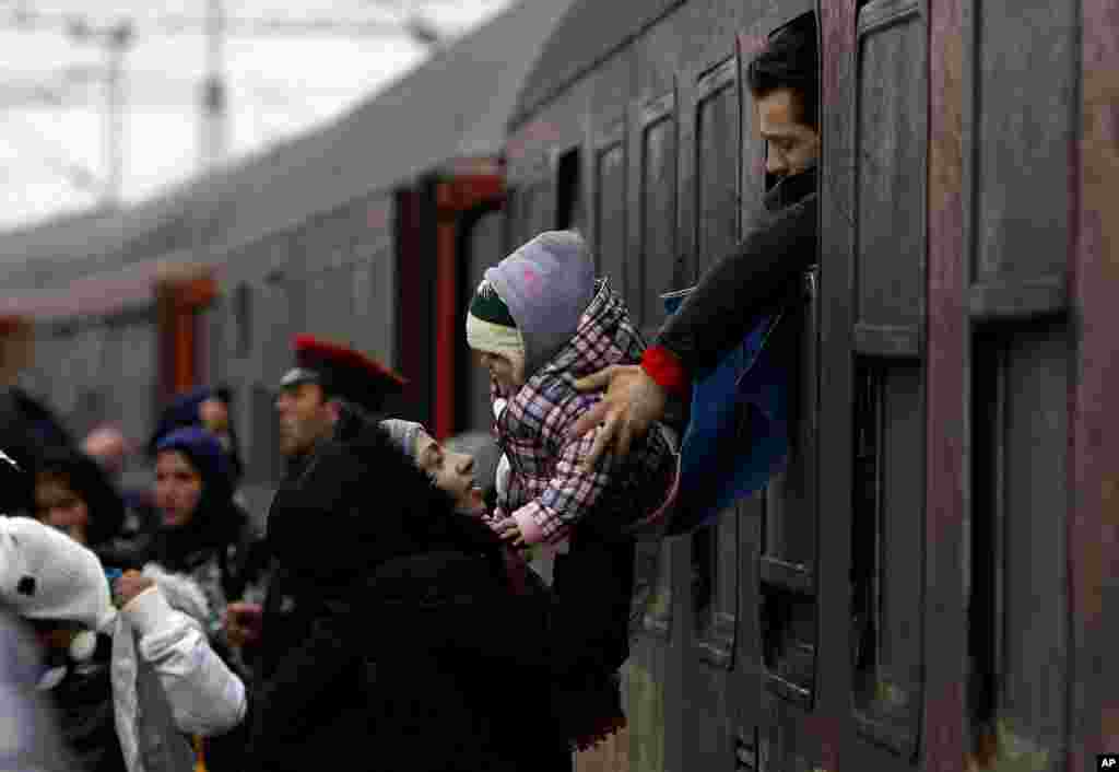 A refugee man passes a baby to a woman from a train window, upon their arrival at the transit center for refugees near northern Macedonian village of Tabanovce.