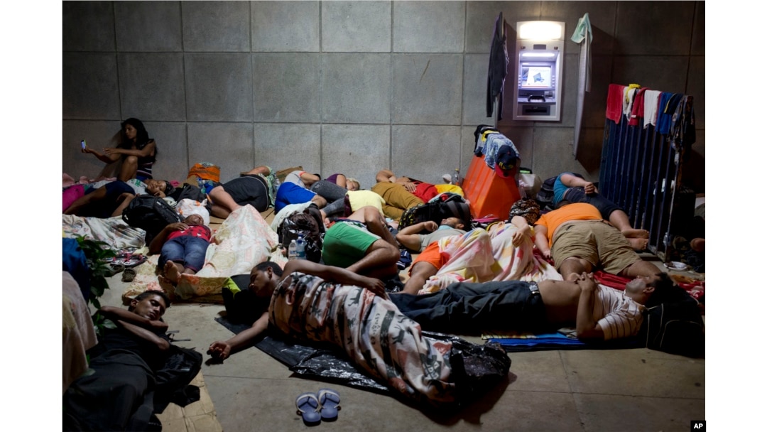 FILE - A Cuban woman migrant uses her cellphone while other Cubans sleep outside the border control building in Penas Blancas, Costa Rica, on the border with Nicaragua, which closed its borders to Cuban migrants, Nov. 21, 2015.