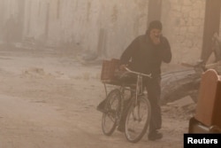 A man covers his face from dust as he walks with a bicycle after a strike on the rebel held besieged al-Shaar neighborhood of Aleppo, Syria, Nov. 26, 2016.