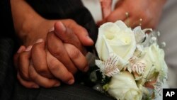 FILE - Newlyweds hold hands during a mass wedding ceremony on Valentine's Day, Thursday, Feb. 14, 2019. (AP Photo/Rebecca Blackwell)