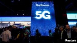 FILE - People walk by a video display promoting 5G connectivity at the Qualcomm booth during the 2019 CES in Las Vegas, Nevada, Jan. 8, 2019.