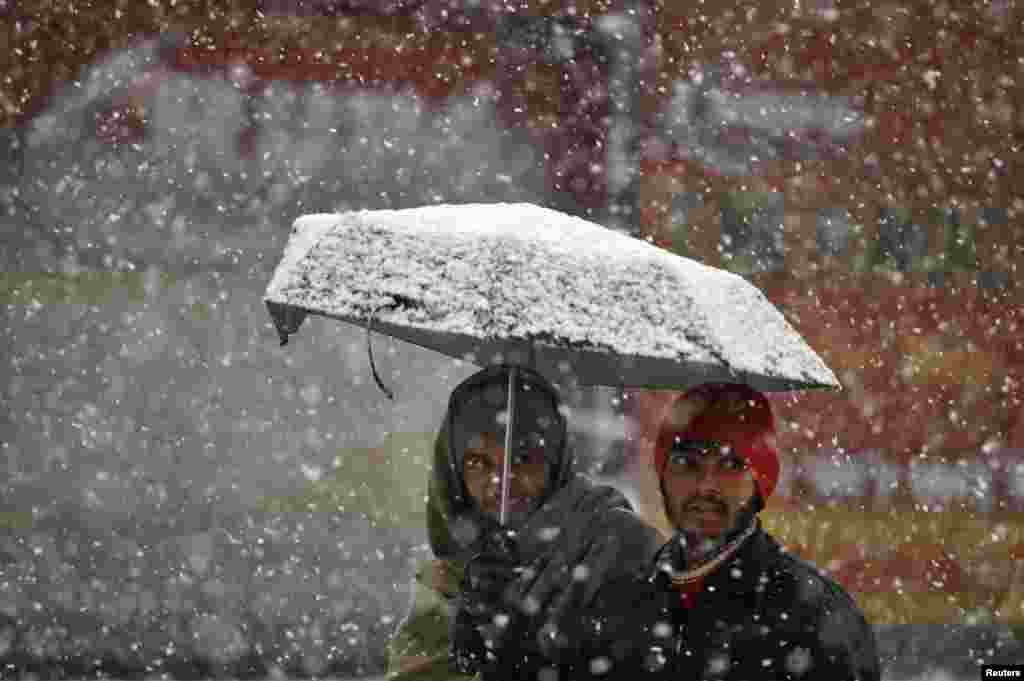 &nbsp;سری نگر میں سرد موسم سرما کی صبح میں برفباری کے دوران دو آدمی ایک چھتری اٹھائے ہوئے جا رہے ہیں۔