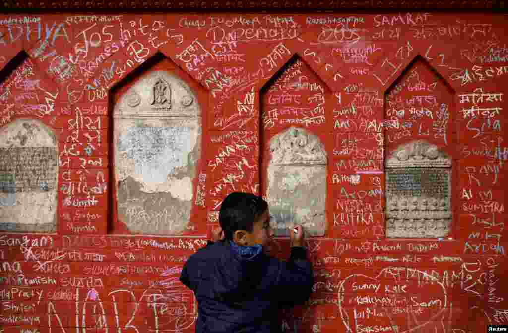 A boy writes on the wall of a Saraswati temple during the Shreepanchami festival in Kathmandu, Nepal.. The festival is in honor of the goddess of education, Saraswati.