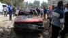 People stand near a damaged car after explosions near Cairo University, April 2, 2014. 