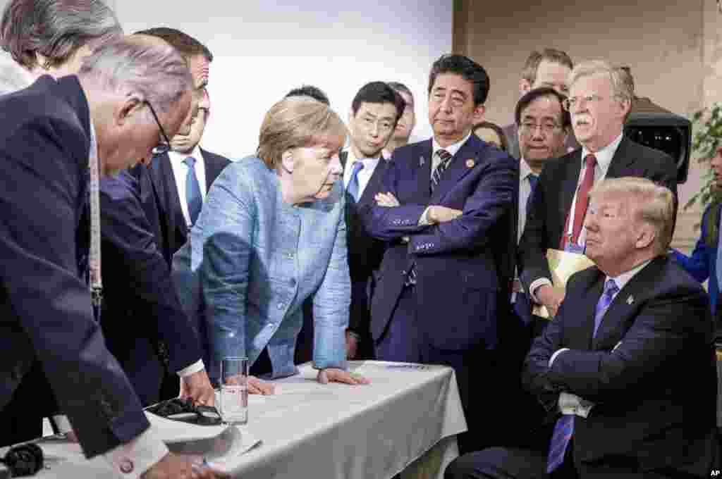 In this photo made available by the German Federal Government, German Chancellor Angela Merkel, center, speaks with U.S. President Donald Trump, seated at right, during the G7 Leaders Summit in La Malbaie, Quebec, Canada, June 9, 2018.