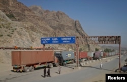 FILE - Men walk near a road sign showing the distance to cities in Afghanistan, as trucks drive past in the northwest town of Torkham, at the border crossing to Pakistan, July 4, 2012.