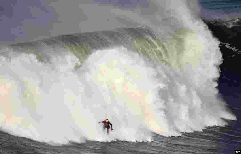 Peselancar Portugis, Nuno Santos mengenakan topi Sinterklas dan membawa biola, sementara berselancar di sela ombak besar di Praia do Norte, Nazare, Portugal.