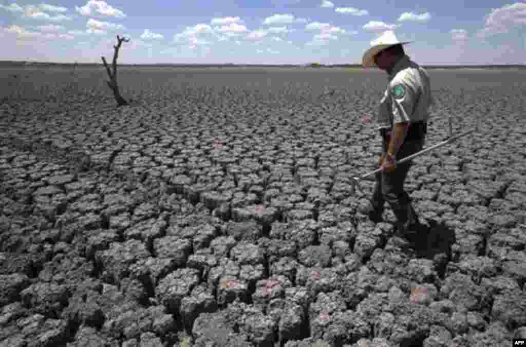 Texas State Park police officer Thomas Bigham walks across the cracked lake bed of O.C. Fisher Lake Wednesday, Aug. 3, 2011, in San Angelo, Texas. A bacteria called Chromatiaceae has turned the 1-to-2 acres of lake water remaining the color red. A combina