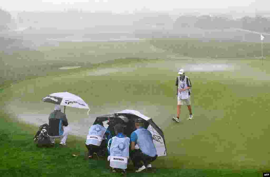 Players and caddies shelter from rain and wind on the flooded second green during the final round of the Portugal Masters golf tournament at the Oceanico Victoria course in Vilamoura, southern Portugal.