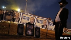An ultra-Orthodox Jew stands near Shas campaign banners that depict party leader Aryeh Deri (top) and near pictures of Rabbi Yisrael Abuhatzeira during an annual pilgrimage to the Rabbi's gravesite in the southern town of Netivot, Israel, Jan. 14, 2013.