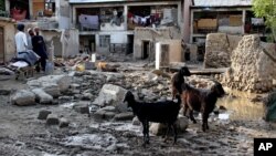 In this Sunday, Aug. 4, 2013 photo, Afghans stand near destroyed homes due to a flood that hit the Surobi district of Kabul, Afghanistan.