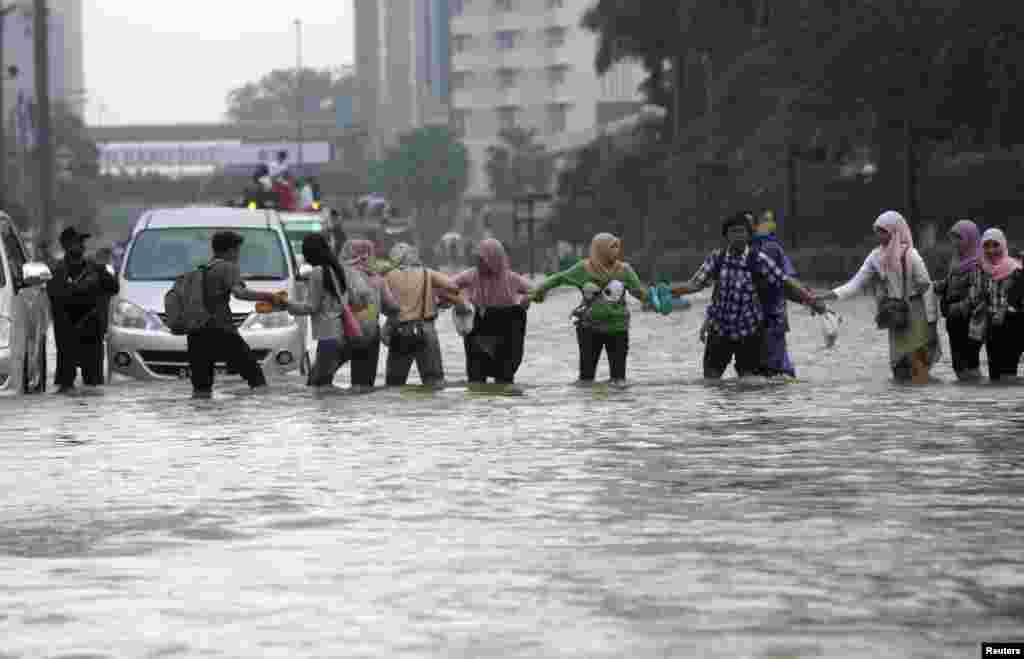 Workers cross a flooded street in the business district in Jakarta, Indonesia, January 17, 2013. 