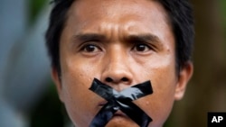FILE - A Myanmar journalist with his mouth sealed with tape, symbolizing the government's recent crackdown on media, protest outside Myanmar Peace Center where President Thein Sein attends a meeting in Yangon, Myanmar, July 12, 2014. 